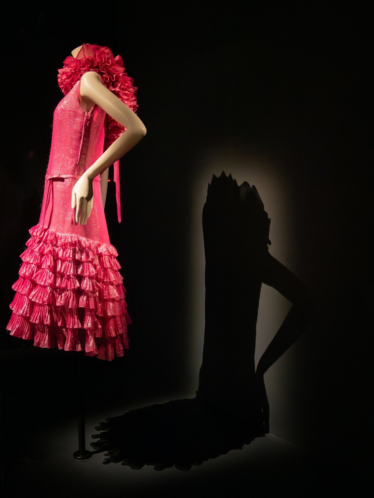 Robe rose à volants sur mannequin, exposition sur fond noir.