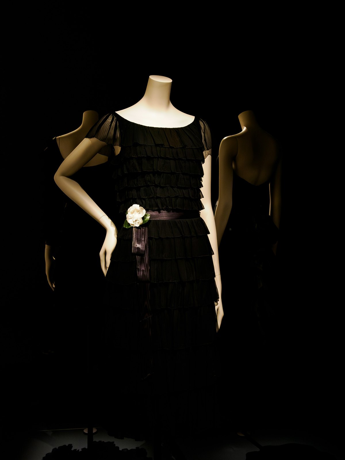 Robe noire à volants exposée sur mannequin, éclairage dramatique.