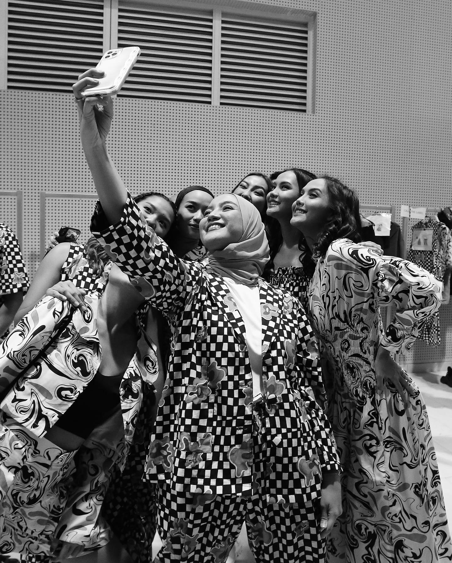Groupe de mannequins prenant un selfie en coulisses, ambiance de défilé.