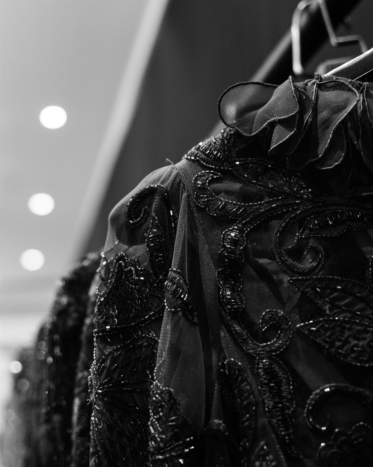 Détail d'une robe de couture noire brodée de perles, sur cintre.