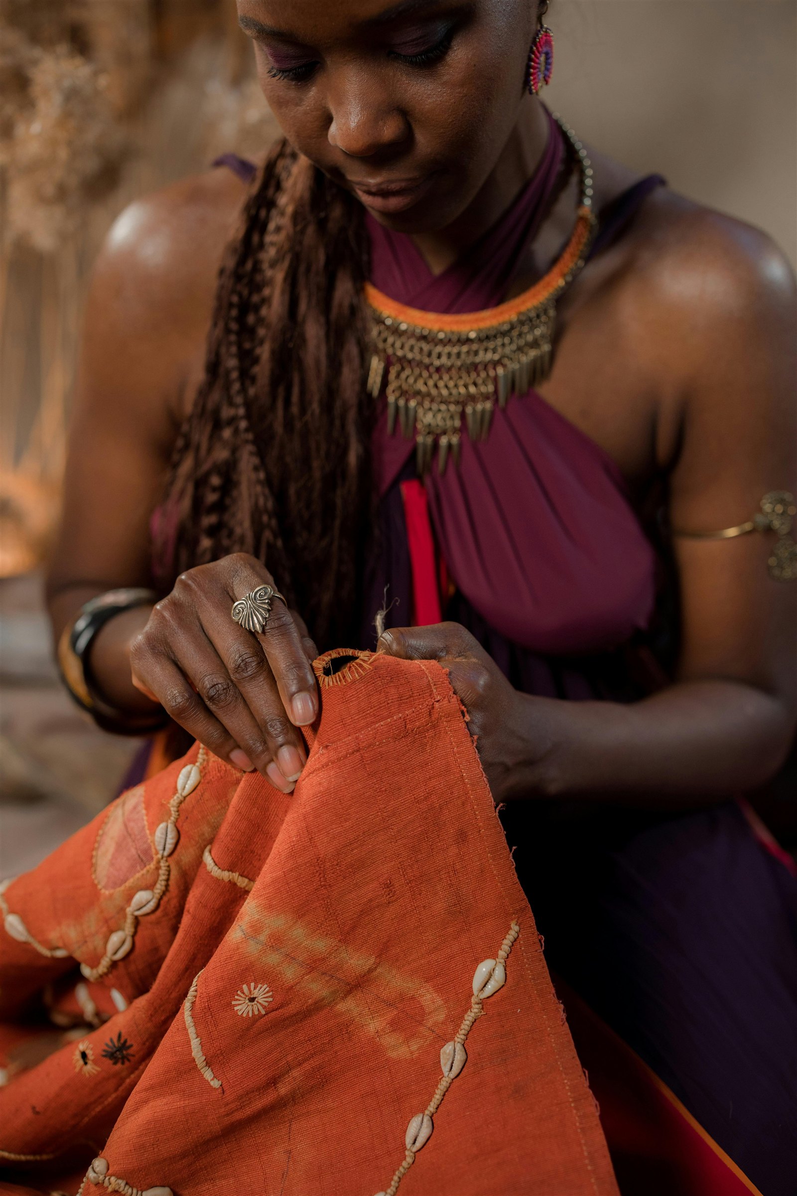 Créatrice cousant un tissu à la main, parée de bijoux traditionnels.