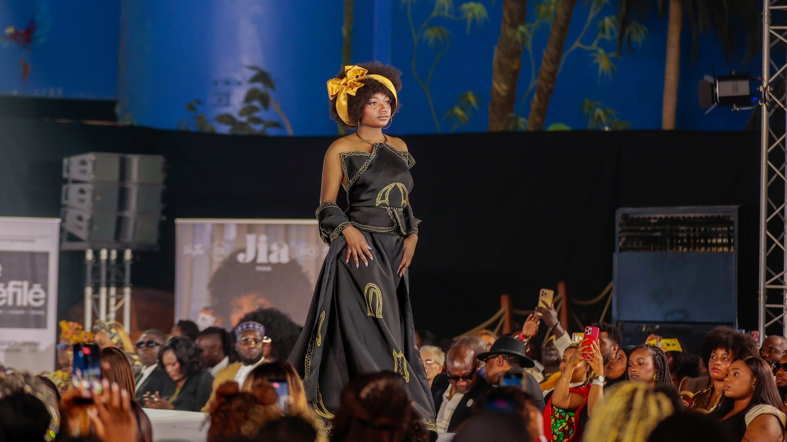 Mannequin en robe noire et or sur le podium de ZE DÉFILÉ 2026, à La Palmeraie, Paris.